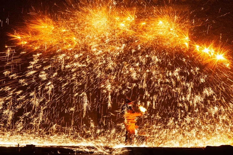 Folk artist Wang De throws molten metal at a stone wall to create sparks